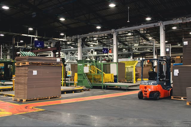 Large stacks of flat-packed corrugated cardboard boxes for fruit packaging stored in the factory warehouse.
